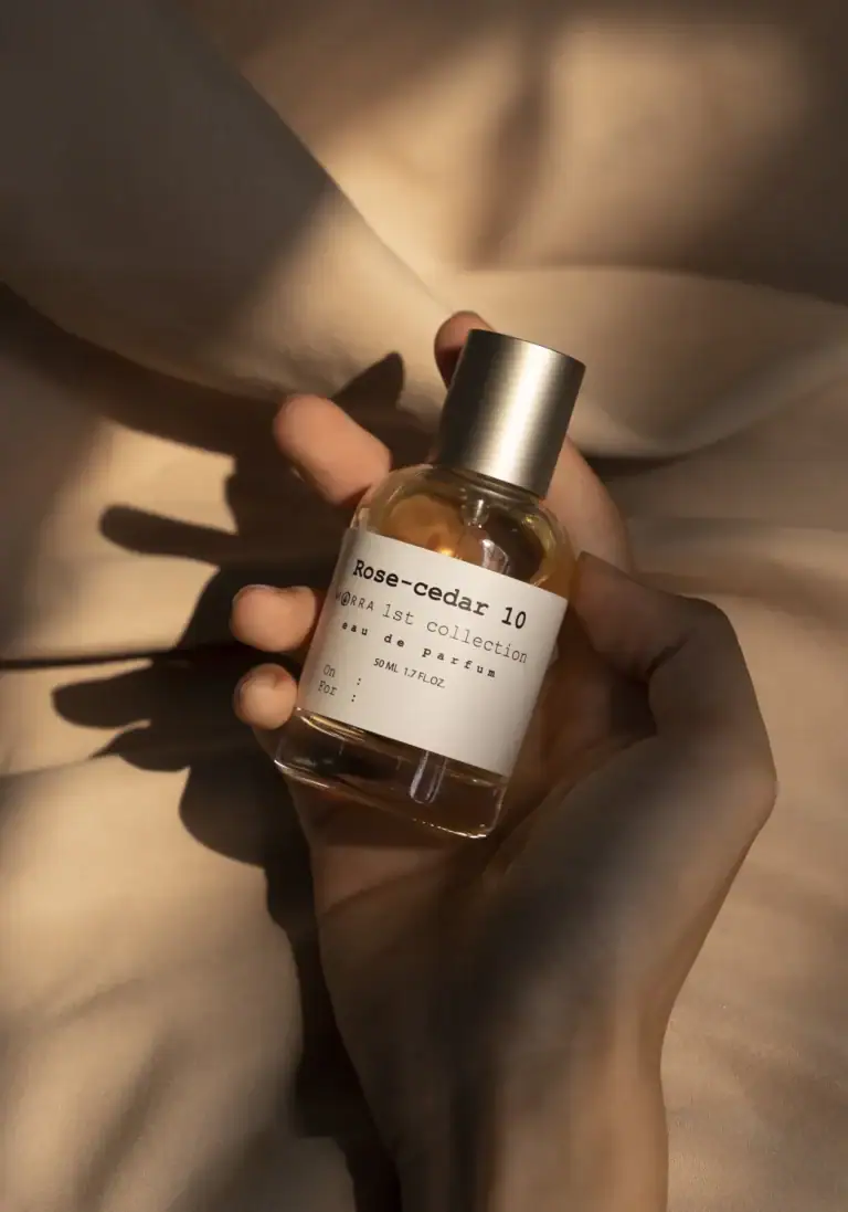Rose cedar body mist by MISTURA in a glass bottle with minimalist label, held in a hand against a soft beige background.