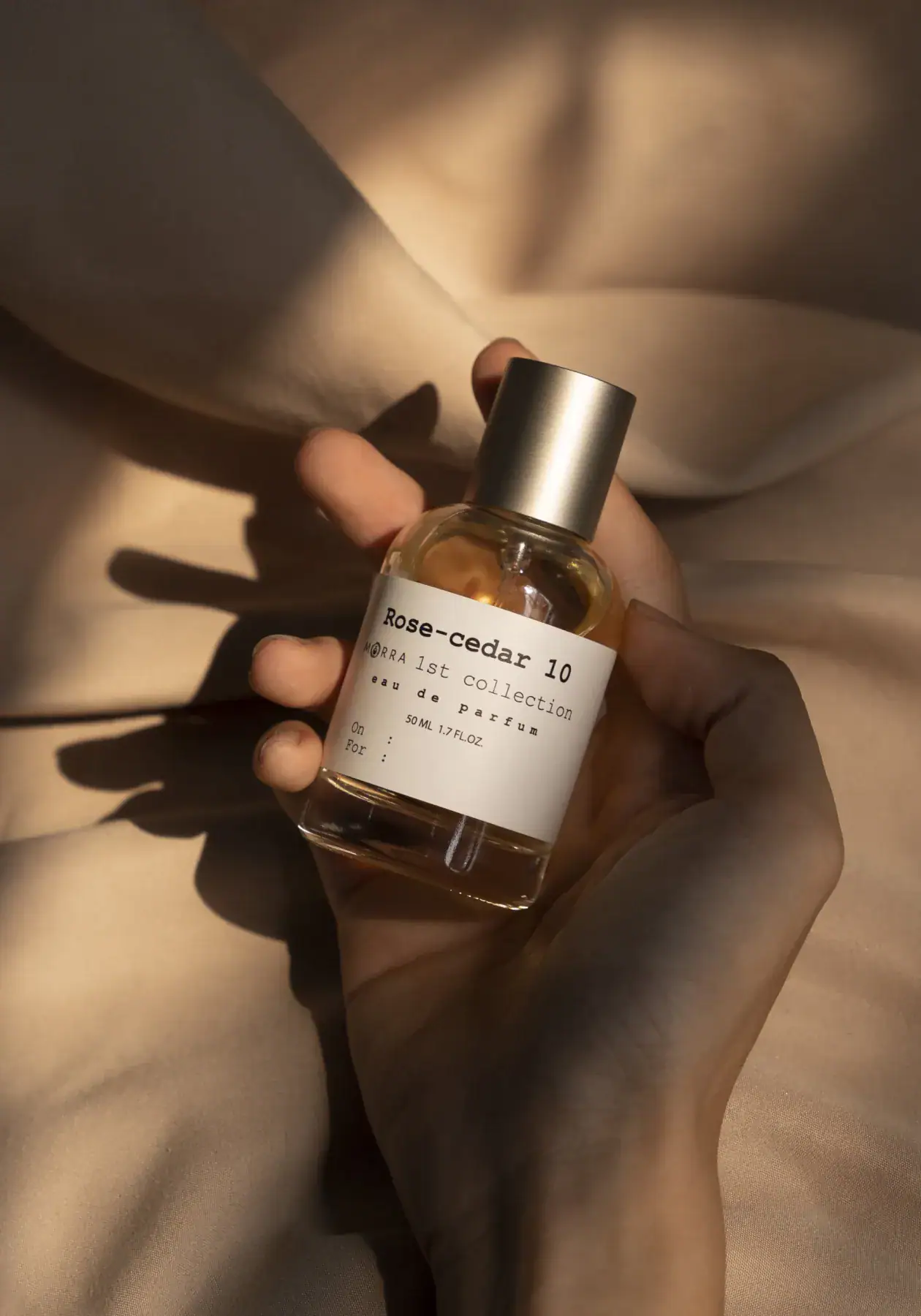Rose cedar body mist by MISTURA in a glass bottle with minimalist label, held in a hand against a soft beige background.